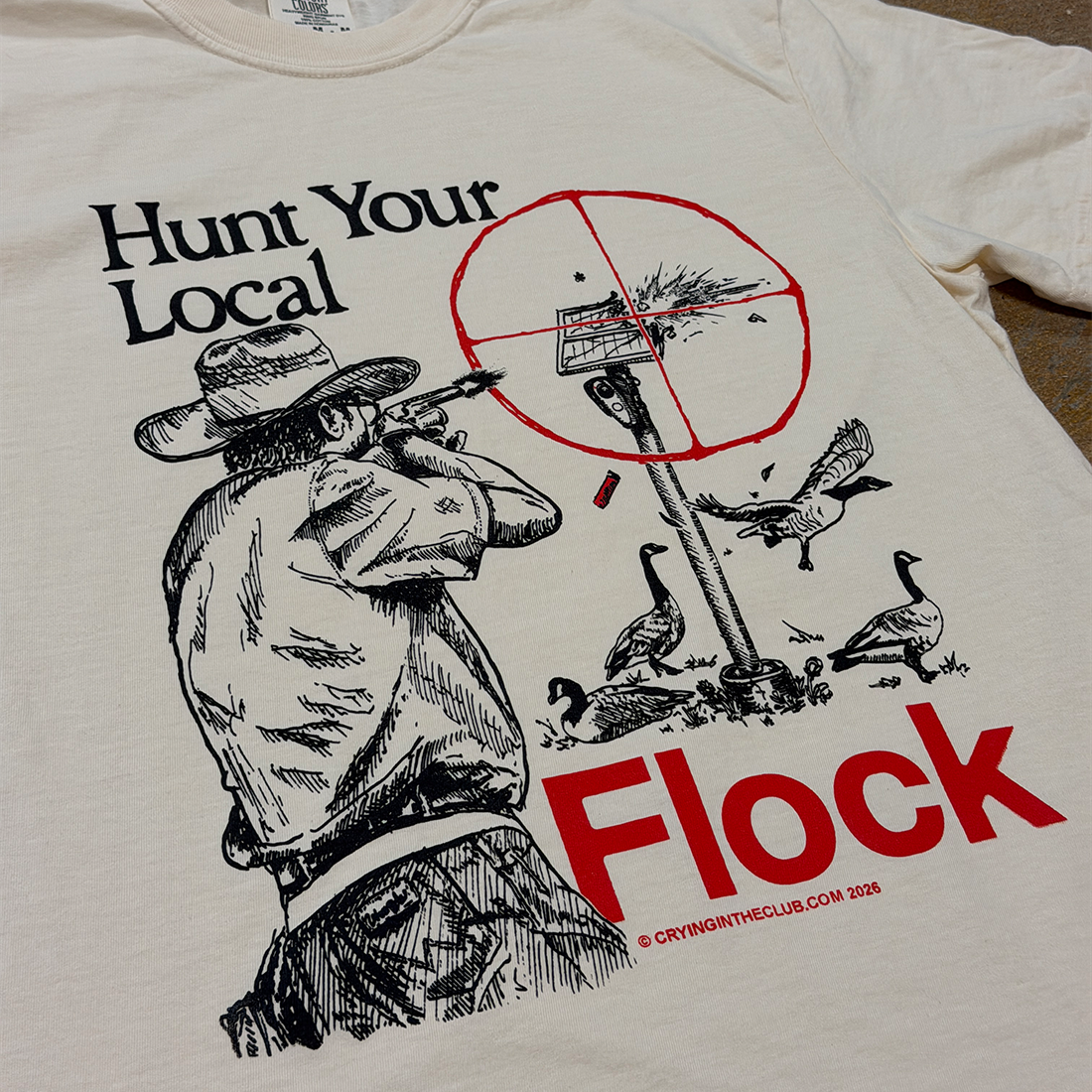 A close-up of a cream-colored graphic t-shirt featuring a black and red illustration of a man hunting geese with the text 'Hunt Your Local Flock'. Crying in the Club T Shirts