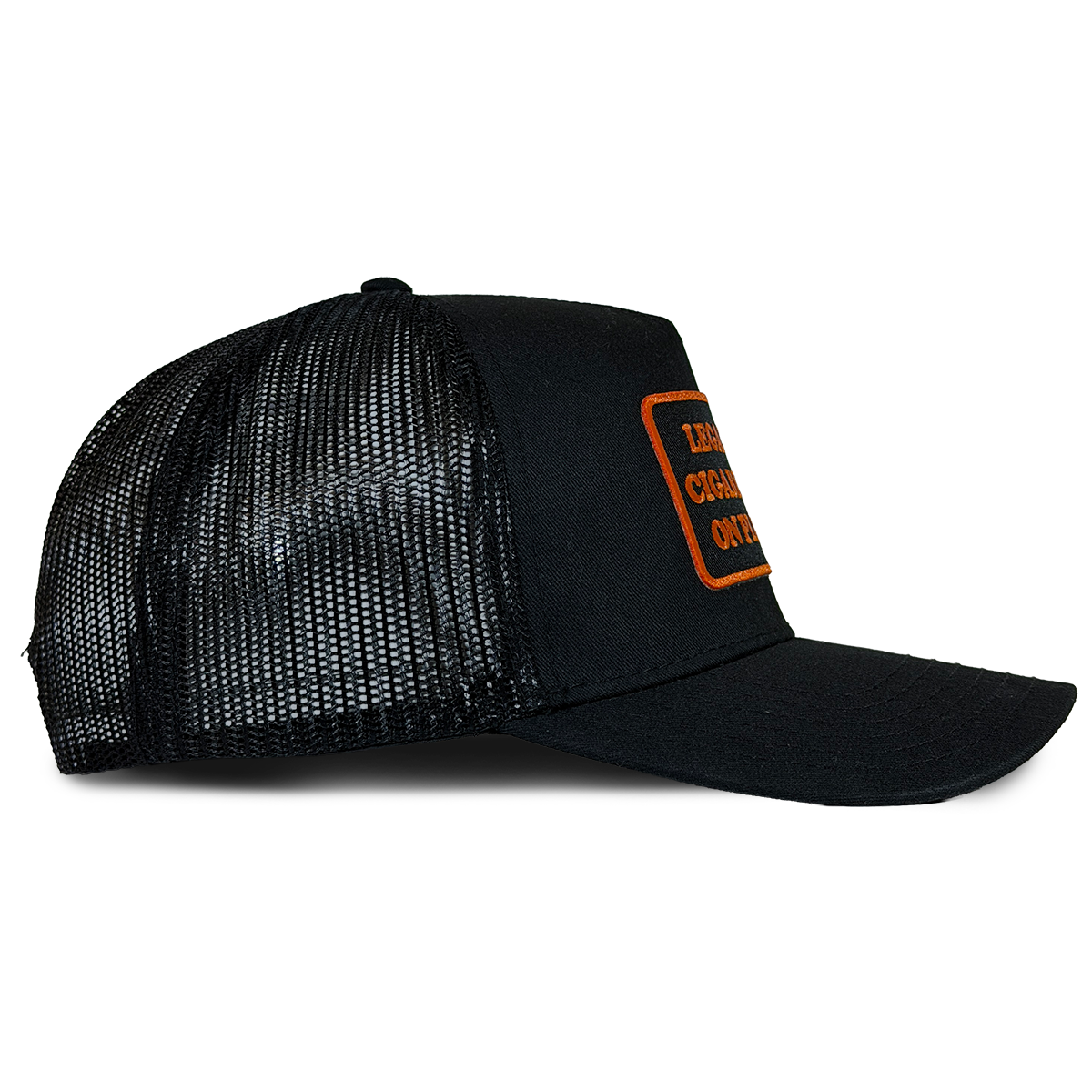 A black trucker-style cap with black mesh back panels and a curved brim, featuring a rectangular orange patch on the side with the text 'LEGALIZE CIGARETTES ON PLANES'. Hat by Crying in the Club Shirts