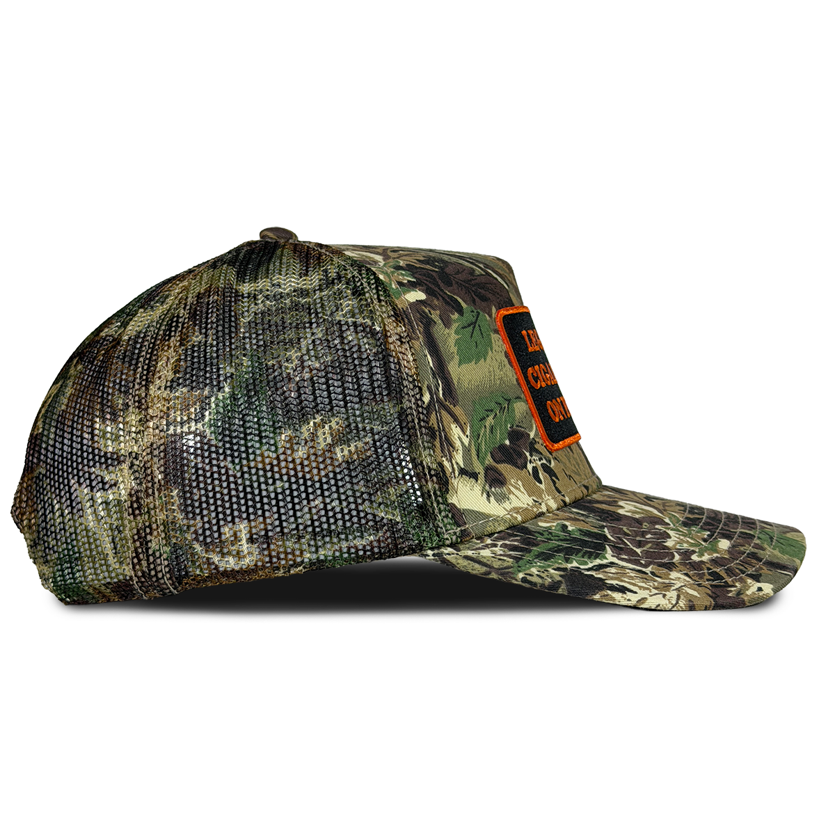 A camouflage trucker cap with a mesh back and a small orange patch on the side, shown against a plain white background. Hat by Crying in the Club Shirts