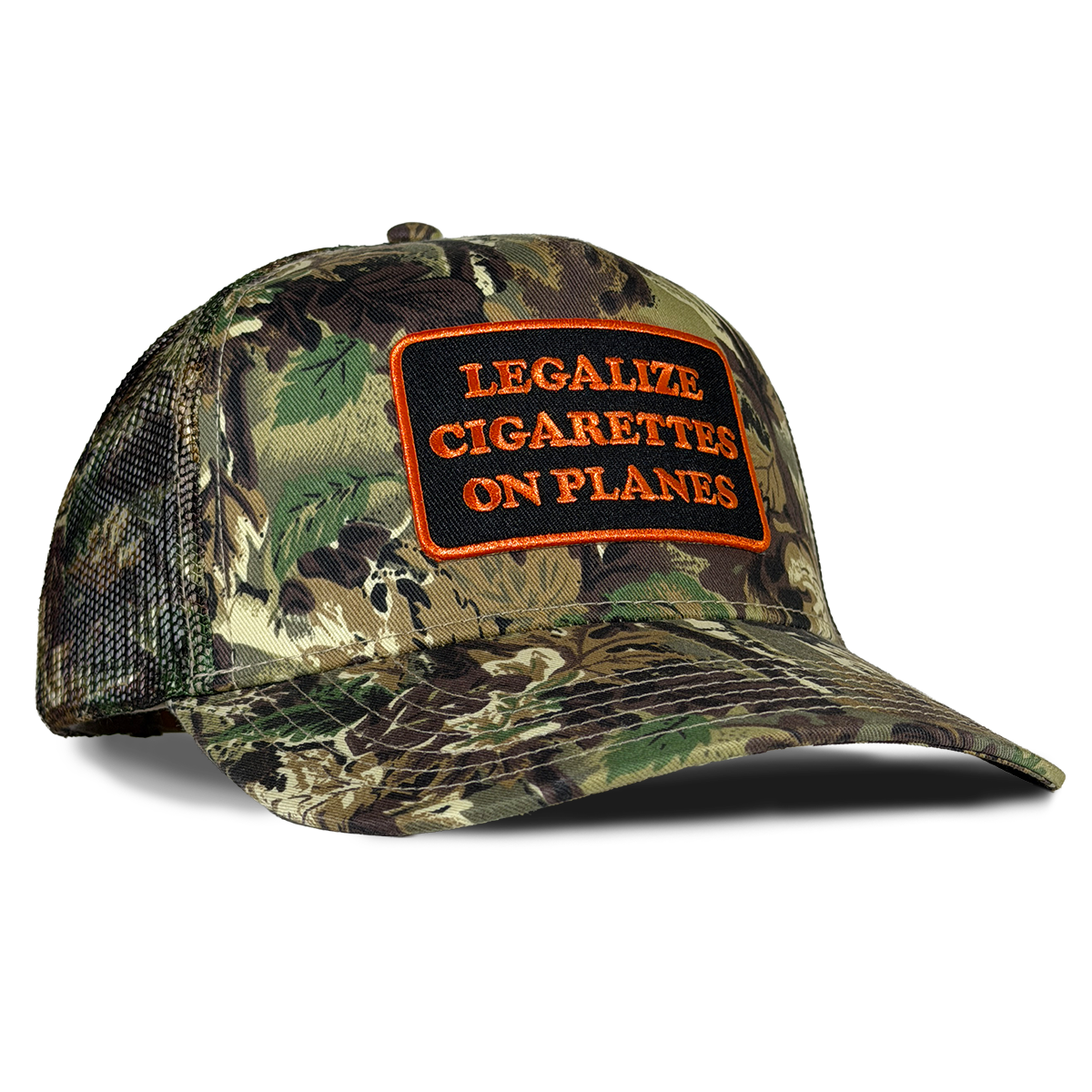 A camouflage trucker hat with a front patch reading 'LEGALIZE CIGARETTES ON PLANES' in orange text on a black background. The hat features a woodland camouflage pattern on the front panels and brim, with green and brown tones, and a black mesh back. Hat by Crying in the Club Shirts