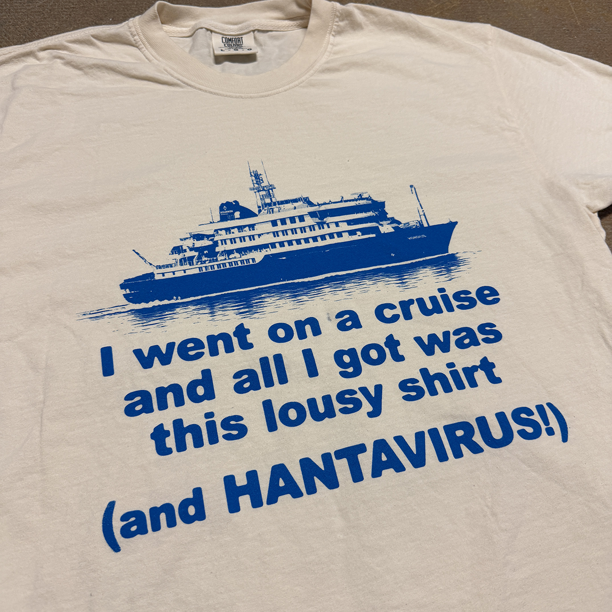 Beige t-shirt with blue graphic of a cruise ship and humorous text on a plain background - I WENT ON A CRUISE AND ALL I GOT WAS THIS LOUSY SHIRT... AND HANTAVIRUS shirt pic crying in the club 