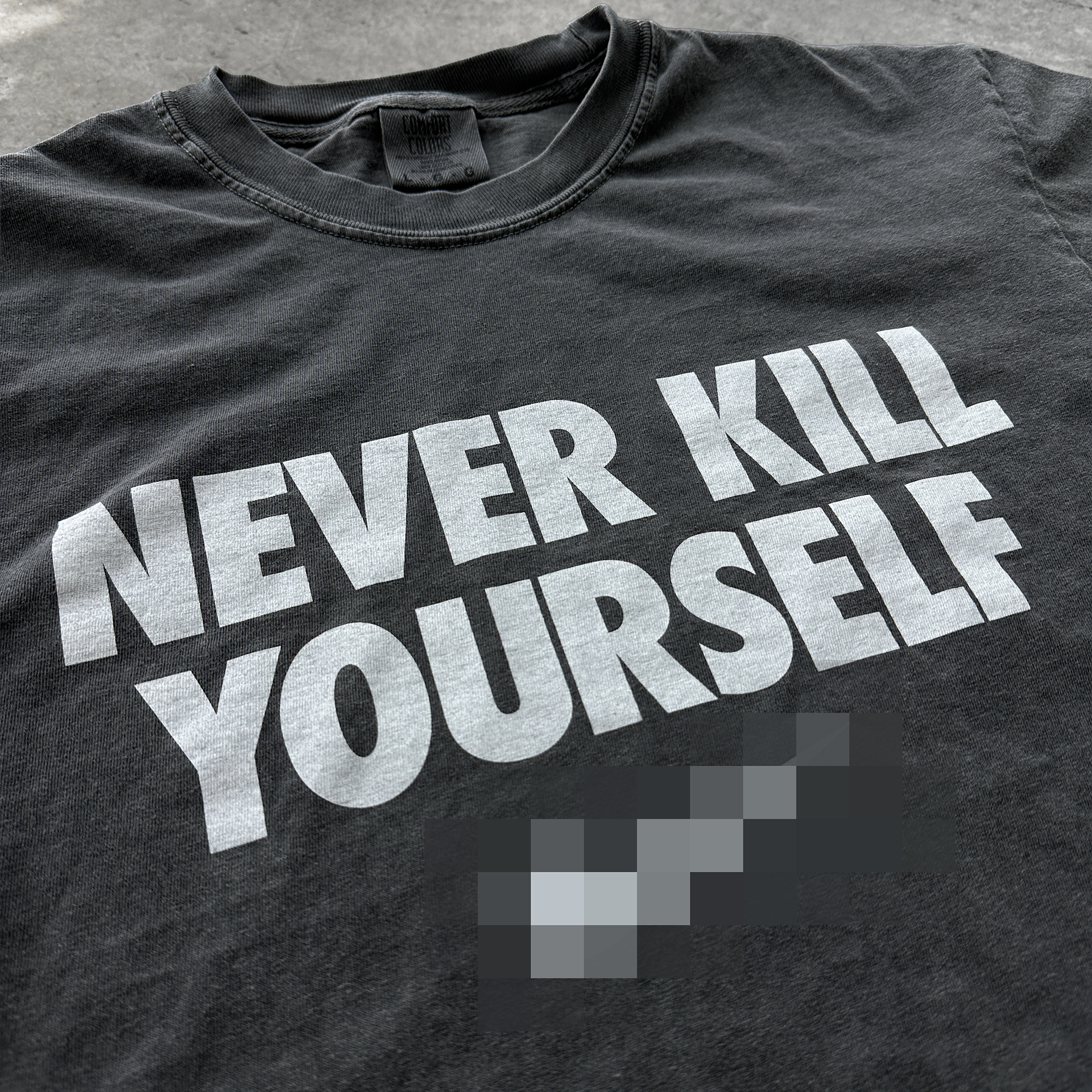 Black t-shirt with 'NEVER KILL YOURSELF' text in white on a gray surface