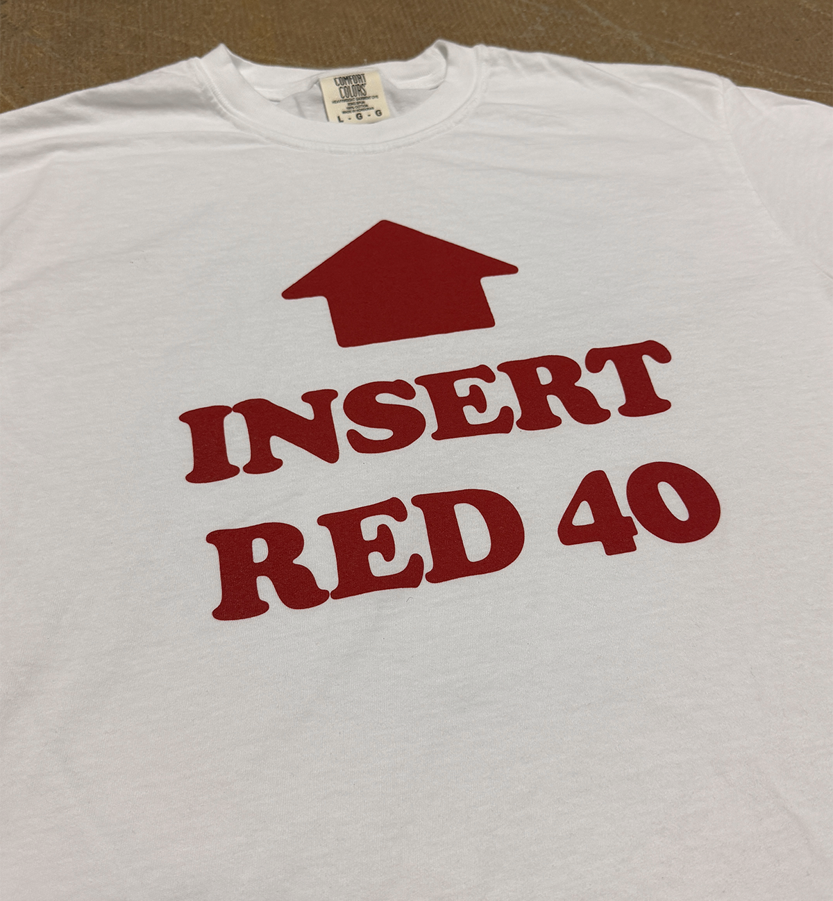 White t-shirt with red text and graphic on a brown background, says INSERT RED 40 with an arrow